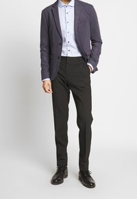 Tmavě modrý blazer, světle modrá košile s knoflíky, černé společenské kalhoty a černé boty. Blazer má jednu kapsu a je ve střihu na míru.