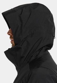 Svart huva jacka i slätt, vattenavvisande material; har hög krage och en lös passform med rynkad textur på luvan.