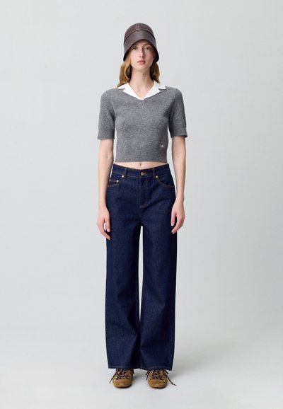 Maglione grigio corto con colletto bianco, abbinato a jeans scuri a gamba larga e scarpe marroni stringate. Design semplice e minimalista.