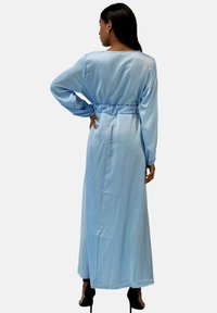 Lyseblå satin kjole med lange ærmer, bælte i taljen og gulvlængde. Glat tekstur og let glans, med rund halsudskæring.