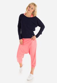 Granatowa bluzka z długim rękawem i szerokim dekoltem, zestawiona z luźnymi różowymi spodniami haremowymi. Całość uzupełniają białe sneakersy.