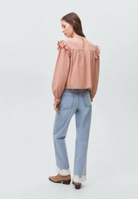 Blusa rosa con spalle a volant, abbinata a jeans a vita alta blu chiaro con orli sfrangiati e stivali alla caviglia marroni.