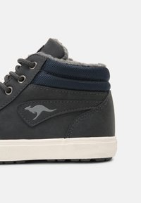 Dunkelgraue High-Top-Schuhe mit glatter Oberfläche, ausgestattet mit einem marineblauen Textilkragen, weißer Gummisohle und einem dezenten Känguru-Logo.