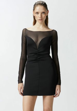 Miniabito nero con design a maniche lunghe trasparenti, caratterizzato da una scollatura a V e dettagli arricciati in vita, che creano una silhouette aderente.