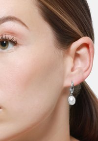 Orecchini a cerchio in argento con un unico pendente a perla bianca. Il design è liscio con una finitura lucida, che pende appena sotto il lobo dell'orecchio.