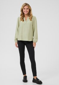 Light green long-sleeve blouse with a V-neck, featuring gathered sleeves and a soft, textured fabric, paired with black fitted pants and black loafers.