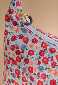 Borsa floreale realizzata in tessuto leggero con uno sfondo blu, fiori rossi e viola e stelle arancioni. La chiusura zip dorata è visibile.