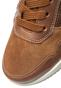 Brown leather sneaker with suede accents, textured surface, round toe, and thick brown laces. Features white stitching and a rubber sole.