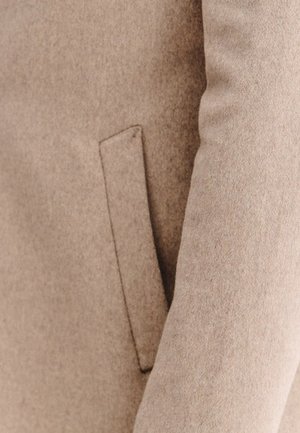 Be�żowy wełniany płaszcz o gładkim, teksturowanym wykończeniu; posiada boczną kieszeń i dopasowany krój, który podkreśla nowoczesny fason.