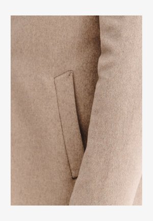 Beżowy wełniany płaszcz o gładkim, teksturowanym wykończeniu; posiada boczną kieszeń i dopasowany krój, który podkreśla nowoczesny fason.