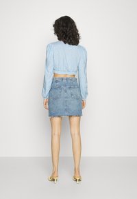 Blusa cropped azul-clara com um padrão floral, combinada com uma saia de denim desgastada. O conjunto apresenta mangas longas e uma bainha levemente desfiada.