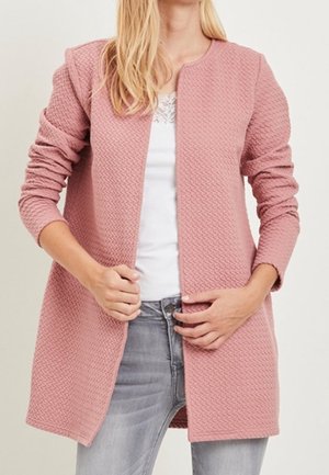 Jasnoróżowy teksturowany płaszcz z długimi rękawami, otwartym przodem i bez zapięć, zestawiony z białą koszulą i szarymi dżinsami.