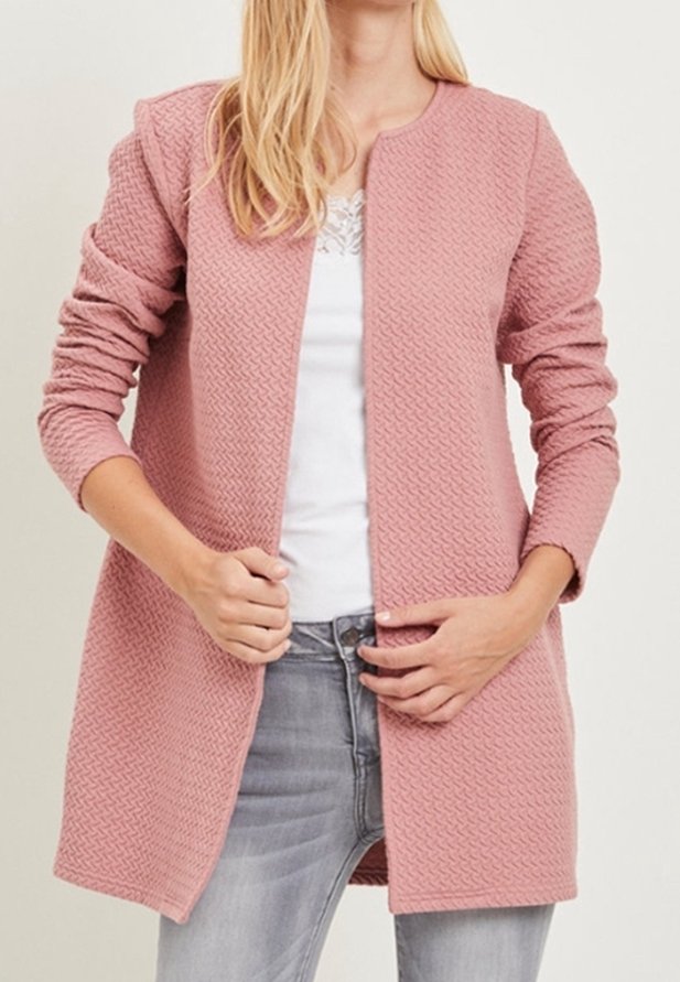 Vaalea vaaleanpunainen teksturoitu takki, jossa on pitkät hihat, avoin etuosasuunnittelu ja ilman kiinnityksiä, yhdistetty valkoiseen paitaan ja harmaisiin farkkuihin.