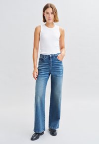 Un haut sans manches blanc associé à un jean bleu large à taille haute. Les jeans présentent un délavage usé, des poches classiques et une coupe droite.