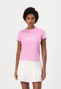 Rosa bomull T-skjorte med rund hals og korte ermer, med hvit tekst som sier "Authentic Original Tommy New York City."