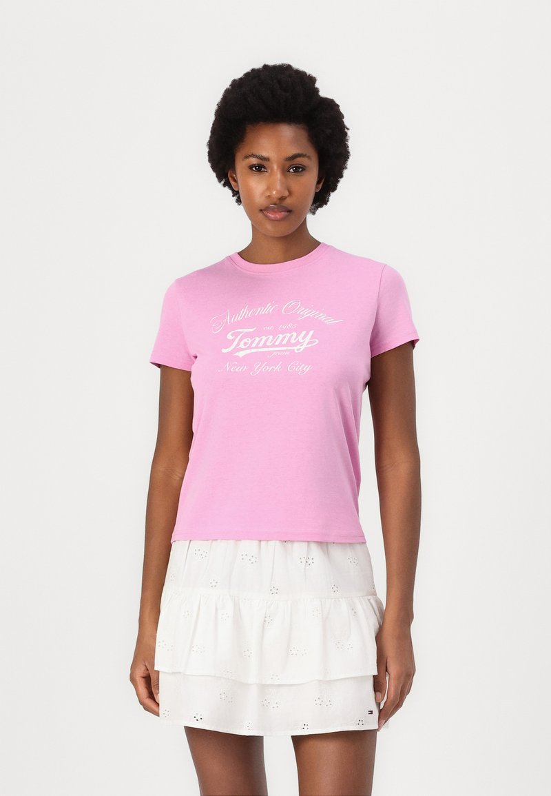 Rosa bomull T-skjorte med rund hals og korte ermer, med hvit tekst som sier "Authentic Original Tommy New York City."