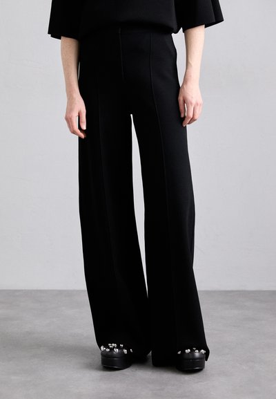 Pantaloni neri a gamba larga con un design su misura, caratterizzati da una texture liscia e dettagli di cucitura sottili, abbinati a scarpe con tacco spesso decorate con borchie.