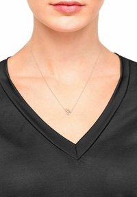 Zilveren ketting met geometrische hanger en veelkleurige accenten, gedragen boven een zwarte V-hals top. Eenvoudig, delicaat ontwerp.
