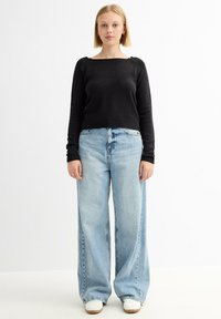 Suéter de punto negro con mangas largas y un escote cuadrado, combinado con jeans de pierna ancha de tiro alto en azul claro y zapatillas blancas.