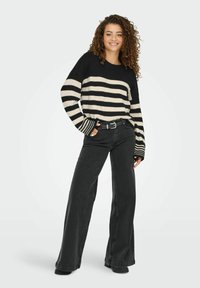 Zwart met crèmekleurige gestreepte gebreide trui met een losse pasvorm, geribbelde manchetten, gecombineerd met hoge taille, wijde zwarte jeans en een zwarte riem.