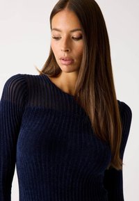 Maglione a coste blu navy con parte superiore a strisce trasparenti. Presenta maniche lunghe, design aderente e texture morbida.