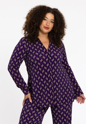 Paarse pyjama set met een geometrisch patroon in oranje en wit, met lange mouwen, een V-halsuitsnijding en een ontspannen pasvorm. Zachte stoftextuur.