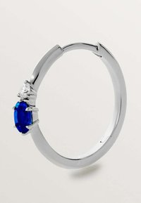 Anillo de plata con una piedra ovalada azul central y dos acentos claros, acabado suave y un diseño elegante y moderno.