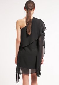 Czarna asymetryczna sukienka z jedną ramiączkiem i warstwowym falbanem z szyfonu. Materiał ma miękką, płynącą teksturę.
