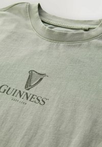 Heleda roheline puuvillane T-särk, millel on tume roheline Guinnessi logo ja tekst "ESTD 1759". Ümar kaelus ja pehme tekstuur, korralikult viimistletud õmblused.