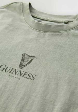 Lichtgroene katoenen T-shirt met een donkergroen Guinness-logo en de tekst "ESTD 1759". Ronde halslijn en een zachte textuur, netjes afgewerkte naden.