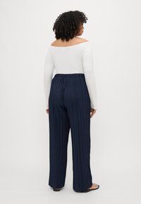Navy pleated wide-leg pants with an elastic waistband, paired with a long-sleeve white top. Smooth texture and relaxed silhouette.