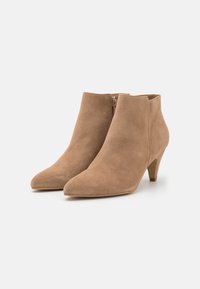 Beige suedestøvler til anklerne med spids tå og kegleformet hæl, der har en lynlås i siden for nemt at tage dem på. Glat tekstur og minimalistisk design.