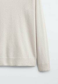 Pull léger beige avec une texture lisse, des poignets et un ourlet côtelés. Présente une coupe décontractée et des manches longues. Matériau doux en tricot.