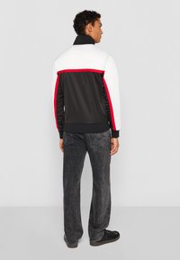 Black jacket with white and red accents, designed with a zip-up collar. Pair of gray jeans with a washed texture. Black shoes complete the look.