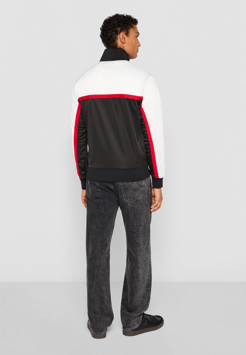 Schwarze Jacke mit weißen und roten Akzenten, entworfen mit einem Reißverschlusskragen. Graue Jeans mit gewaschenem Textur. Schwarze Schuhe runden den Look ab.