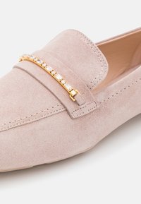 Mocassin en daim rose clair avec bout pointu et barre dorée ornée de cristaux rectangulaires clairs sur le cou-de-pied.