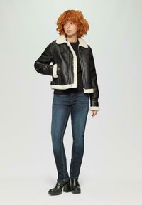 Schwarze Lederjacke mit weißem Lammfellkragen und -ärmeln, kombiniert mit dunkelblauen Jeans und schwarzen Plateaustiefeln. Einfaches Design, ohne Muster.