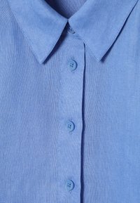 Chemise bleu clair à boutons avec un col pointu et trois boutons visibles à l'avant.