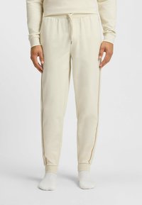 Lichtbeige joggers gemaakt van zachte stof, met een trekkoord in de taille en contrasterende zijstrepen. Strakke boorden bij de enkels.
