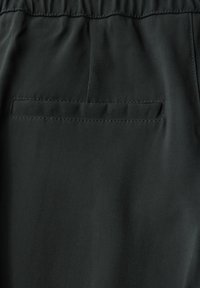 Svart tyg, slät textur, med en enkel sydd ficka på baksidan, elastisk midjeband med rynkdetaljer ovanför.