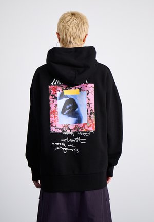 Sudadera negra con una gran gráfica en la parte posterior, con un diseño en rosa y azul, acentos texturizados y texto blanco escrito a mano.