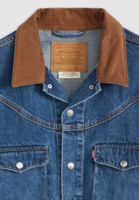 Chaqueta de mezclilla azul con cuello de pana marrón, botones de metal a presión, dos bolsillos frontales con solapa y etiqueta de cuero con la marca Levi's en el interior del cuello.