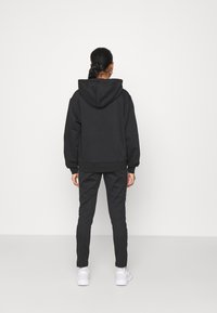 Zwarte hoodie met een buidelzak, geribbelde boorden en zoom, gecombineerd met zwarte trainingsbroeken met witte zijstrepen, gedragen met witte sneakers.