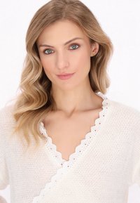 Cardigan bianco lavorato a maglia con bordo in pizzo a scallop lungo il collo. Texture morbida e vestibilità rilassata, caratterizzata da un design a scollatura a V.