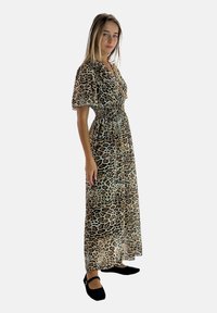 Robe maxi à imprimé léopard avec des manches courtes en volants, taille smockée et tissu fluide ; associée à des ballerines noires.