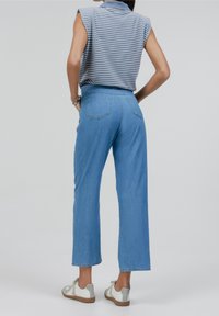 Vaqueros de pierna ancha en azul claro con cintura alta y dos bolsillos traseros, combinados con un top sin mangas de rayas grises y blancas y zapatos casuales.