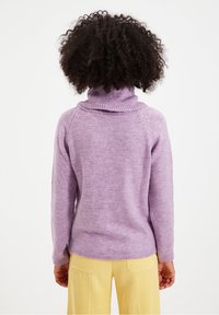 Pull violet à col roulé avec un col côtelé, une texture douce et une coupe décontractée, porté avec un pantalon en velours côtelé jaune.