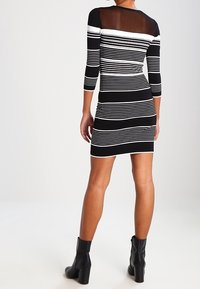 Abito bodycon a righe bianche e nere con maniche a tre quarti, caratterizzato da un pannello in rete nera trasparente sulla schiena. Indossato con stivaletti neri alla caviglia.