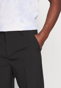 Black trousers with a smooth fabric, featuring side pockets and a straight cut. Accompanied by a plain light blue and white tie-dye t-shirt.