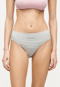 Γυναίκα που φορά γκρι εσώρουχα με την επιγραφή «Wednesday» μπροστά και ένα ανοιχτό ροζ υφασμάτινο σουτιέν, παρουσιασμένη από τη μέση μέχρι τους άνω μηρούς.